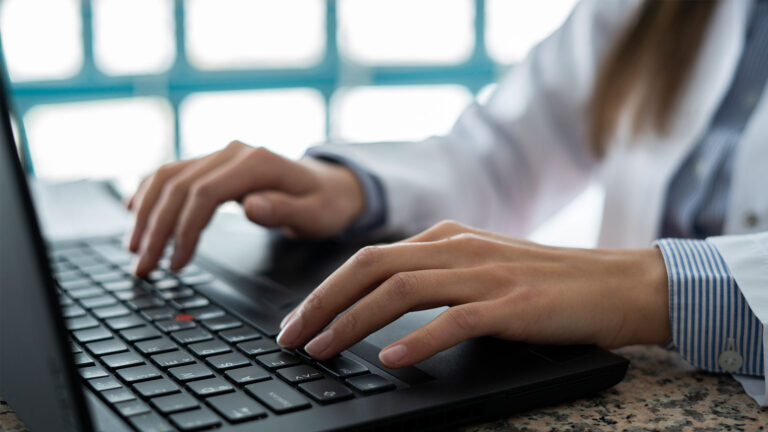 Pharmacy professional closeup typing on laptop