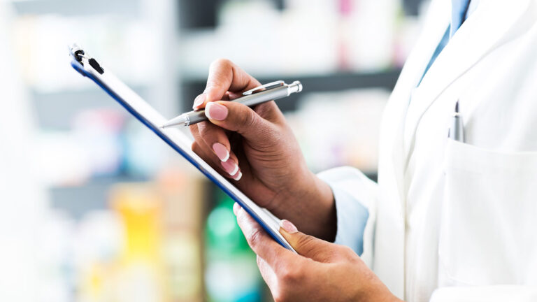 Closeup of pharmacy professional writing on clipboard